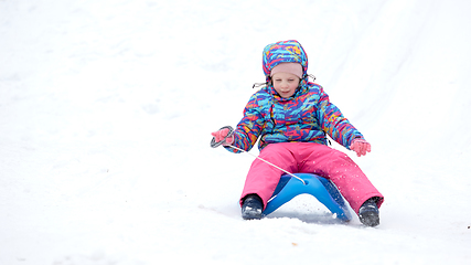 Image showing Cheerful girl riding a sled downhill on a snow covered sledge trail in a white sunny winter mountain landscape