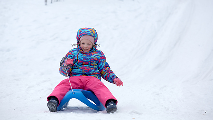 Image showing Cheerful girl riding a sled downhill on a snow covered sledge trail in a white sunny winter mountain landscape