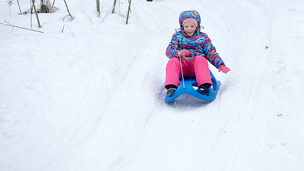 Image showing Cheerful girl riding a sled downhill on a snow covered sledge trail in a white sunny winter mountain landscape