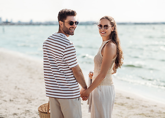 Image showing happy couple with picnic basket walking on beach