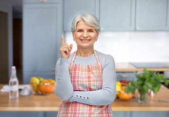 Image showing smiling senior woman in apron pointing finger up