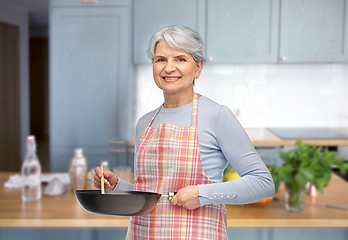 Image showing smiling senior woman in apron with frying pan