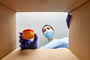 Image showing woman in mask unpacking parcel box with cosmetics