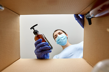 Image showing woman in mask unpacking parcel box with cosmetics