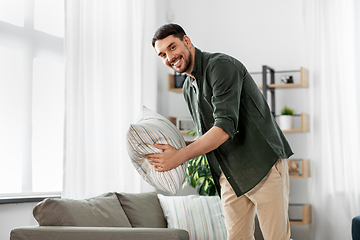 Image showing happy smiling man arranging sofa cushions at home