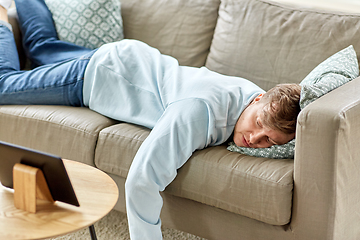 Image showing bored man with tablet pc lying on sofa at home