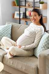 Image showing happy pregnant asian woman sitting on sofa at home