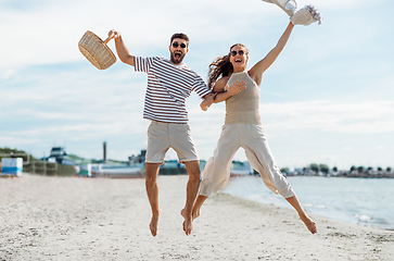 Image showing happy couple with picnic basket jumping on beach