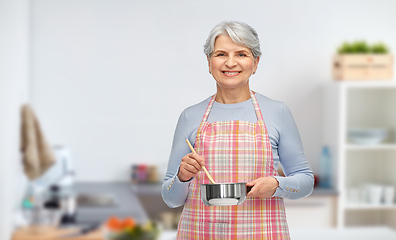 Image showing old woman in kitchen apron with pot cooking food