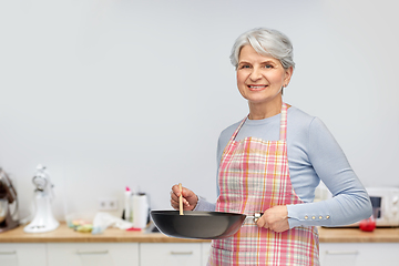 Image showing smiling senior woman in apron with frying pan