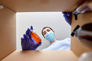 Image showing woman in mask unpacking parcel box with cosmetics