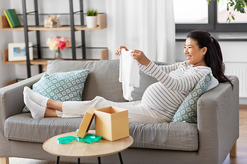 Image showing happy pregnant woman with baby's bodysuit at home