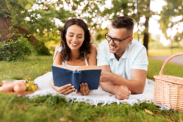 Image showing happy couple reading book on picnic at summer park