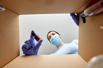 Image showing woman in mask unpacking parcel box with cosmetics