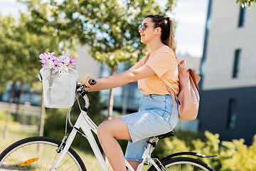 Image showing happy woman with earphones riding bicycle in city