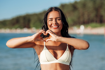 Image showing smiling young woman in showing hand heart on beach