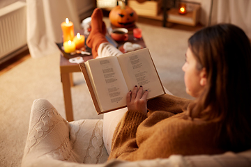 Image showing young woman reading book at home on halloween