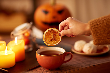 Image showing hand adding dry orange to cup of tea on halloween