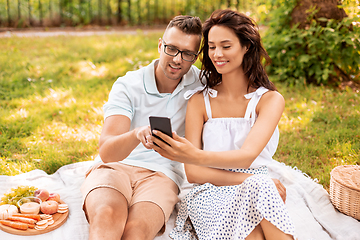 Image showing happy couple with smartphone at picnic in park