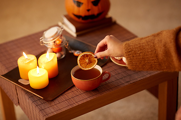 Image showing hand adding dry orange to cup of tea on halloween