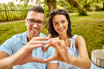 Image showing happy couple making finger heart at summer park