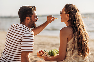 Image showing happy couple with food having picnic on beach