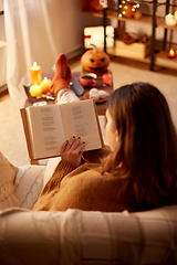 Image showing young woman reading book at home on halloween