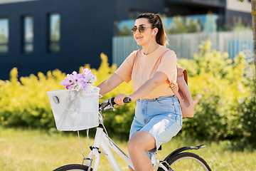 Image showing happy woman with earphones riding bicycle in city
