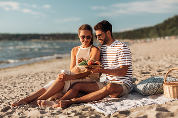 Image showing happy couple with food having picnic on beach