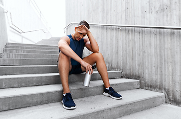 Image showing tired sportsman with bottle sitting on stairs