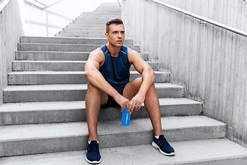 Image showing tired sportsman with bottle sitting on stairs