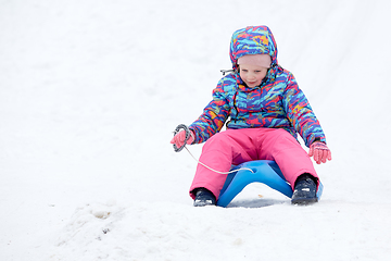 Image showing Cheerful girl riding a sled downhill on a snow covered sledge trail in a white sunny winter mountain landscape