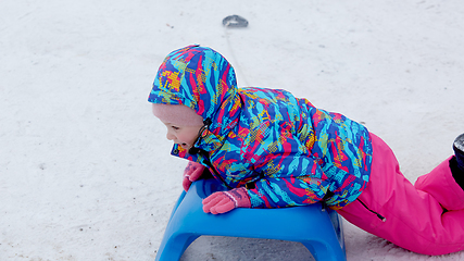 Image showing Cheerful girl riding a sled downhill on a snow covered sledge trail in a white sunny winter mountain landscape