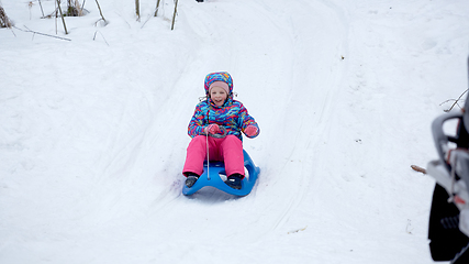 Image showing Cheerful girl riding a sled downhill on a snow covered sledge trail in a white sunny winter mountain landscape