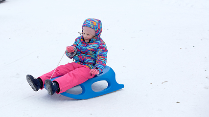 Image showing Cheerful girl riding a sled downhill on a snow covered sledge trail in a white sunny winter mountain landscape