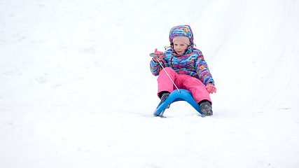 Image showing Cheerful girl riding a sled downhill on a snow covered sledge trail in a white sunny winter mountain landscape