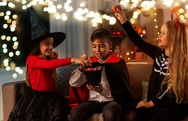 Image showing kids in halloween costumes sharing candies at home