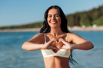 Image showing smiling young woman in showing hand heart on beach