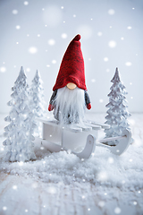 Image showing Cute Christmas gnome is sitting on sled, winter country with white trees 