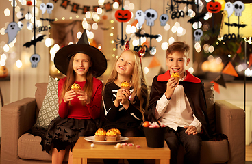 Image showing kids in halloween costumes eating cupcakes at home