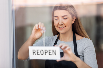 Image showing happy woman hanging reopen banner to door glass