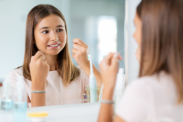 Image showing teenage girl with floss cleaning teeth at bathroom