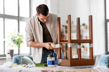 Image showing man sticking adhesive tape to table for repainting