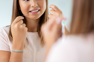 Image showing teenage girl with floss cleaning teeth at bathroom