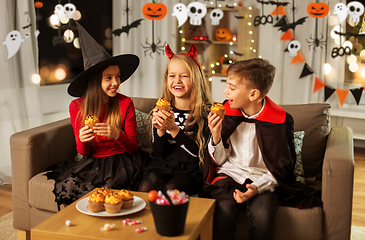 Image showing kids in halloween costumes eating cupcakes at home