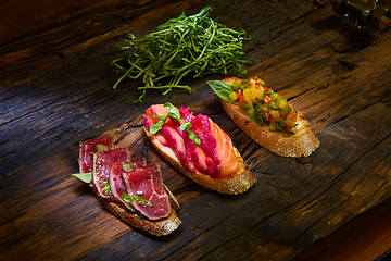 Image showing Assorted bruschetta with roast beef, vegetables and lightly salted salmon with greens leaves on wooden background.