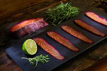 Image showing Sliced salmon fillet, salted with beetroot juice, served on whole wheat with salad leaves, sea salt and pepper over metal surface. Top view