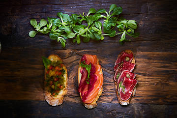 Image showing Assorted bruschetta with roast beef, vegetables and lightly salted salmon with greens leaves on wooden background.