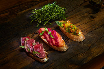 Image showing Assorted bruschetta with roast beef, vegetables and lightly salted salmon with greens leaves on wooden background.