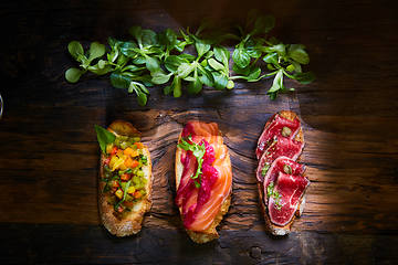 Image showing Assorted bruschetta with roast beef, vegetables and lightly salted salmon with greens leaves on wooden background.